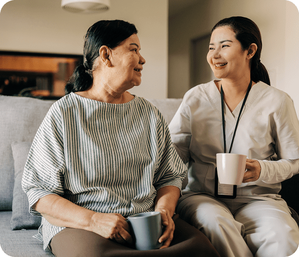 Woman and caregiver smiling with coffee mugs